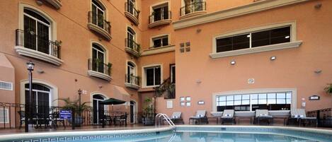 A hotel pool area with a pool, lounge chairs, and a staircase leading to the upper floors.