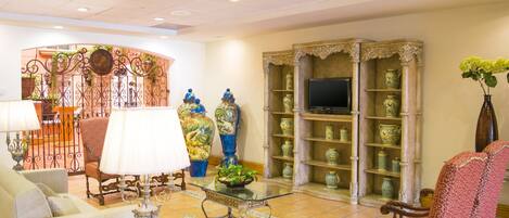 A hotel lobby with a seating area, a television on a stand, and a decorative display of vases.