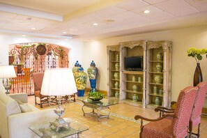 Un vestíbulo de hotel con una zona de estar, un televisor sobre un soporte y una exhibición decorativa de jarrones.