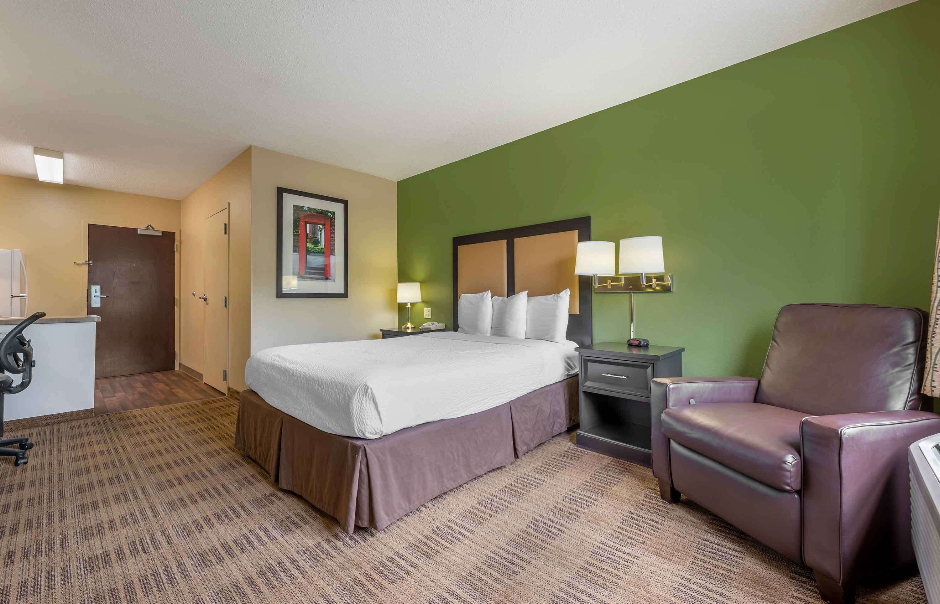 A hotel room with a bed, a desk, a chair, and a nightstand with lamps.