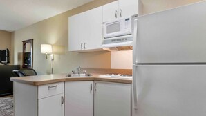 Een kleine keuken met witte kastjes, een magnetron, een koelkast, een spoelbak en een klein aanrecht.