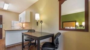 Een compacte hotelkamer met kitchenette, een eettafel met twee stoelen, een grote spiegel en een wandlamp.