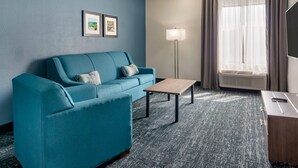 A modern hotel room with a teal sofa, a small wooden table, a floor lamp, and a large window with curtains. - Comfort Inn & Suites Troutville-Roanoke North (Troutville)