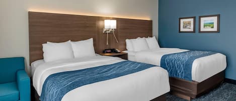 A hotel room with two beds, a nightstand, a blue chair, and two framed pictures on the wall.