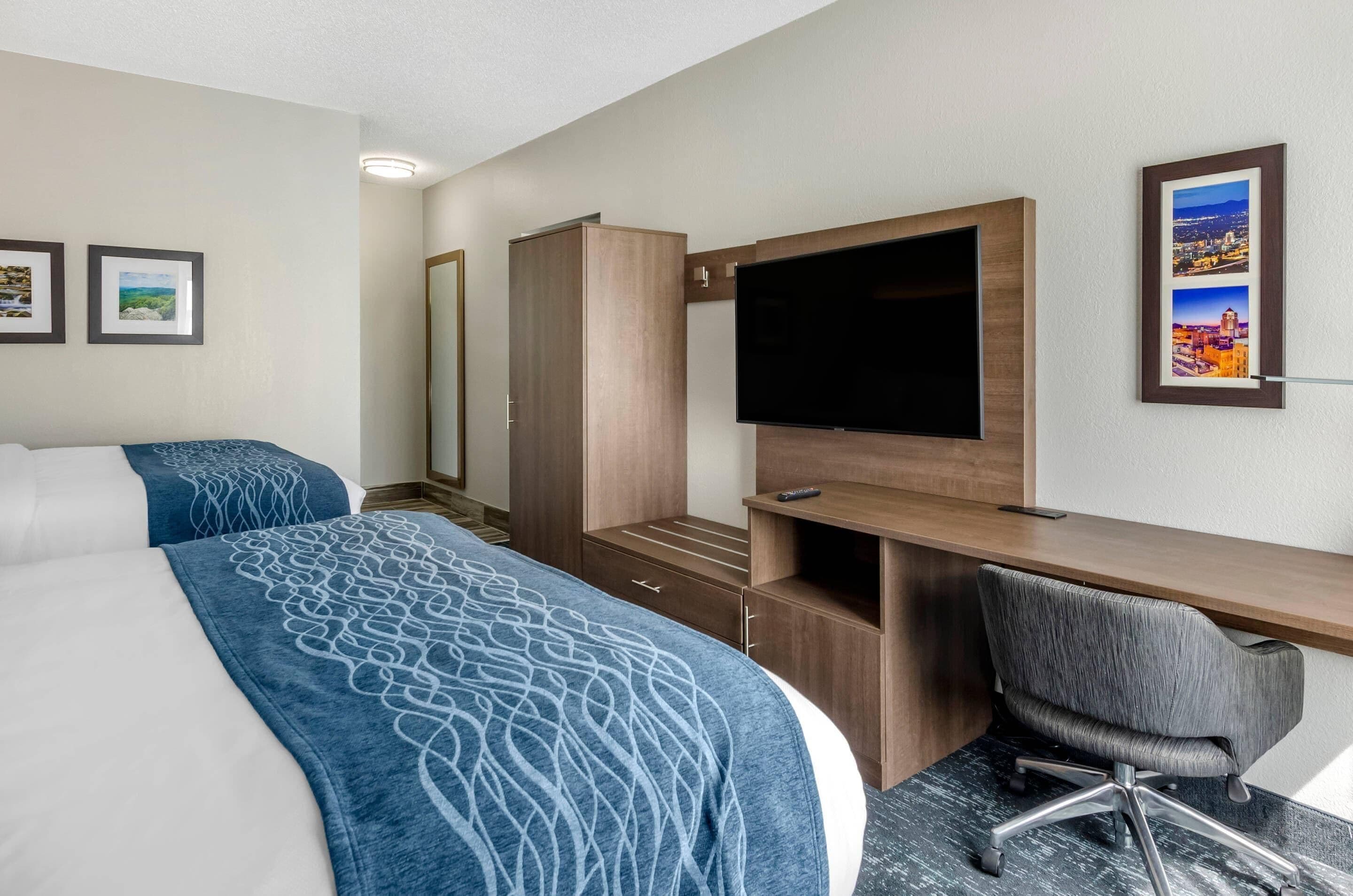 Une chambre d’hôtel avec deux lits, un bureau avec une chaise, un téléviseur à écran plat et des tableaux encadrés au mur.