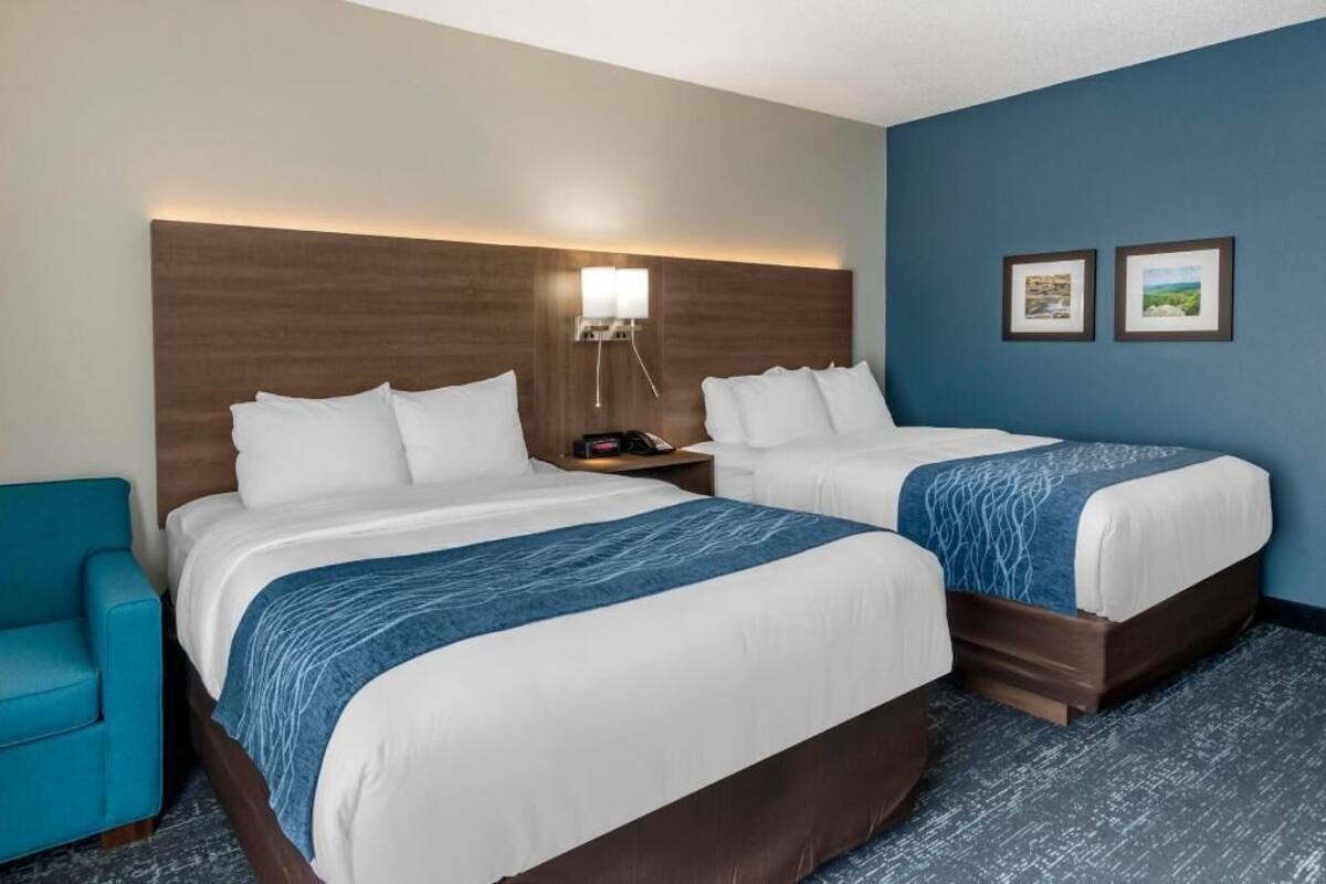 A hotel room with two beds, a nightstand, a lamp, a chair, and two framed pictures on the wall.