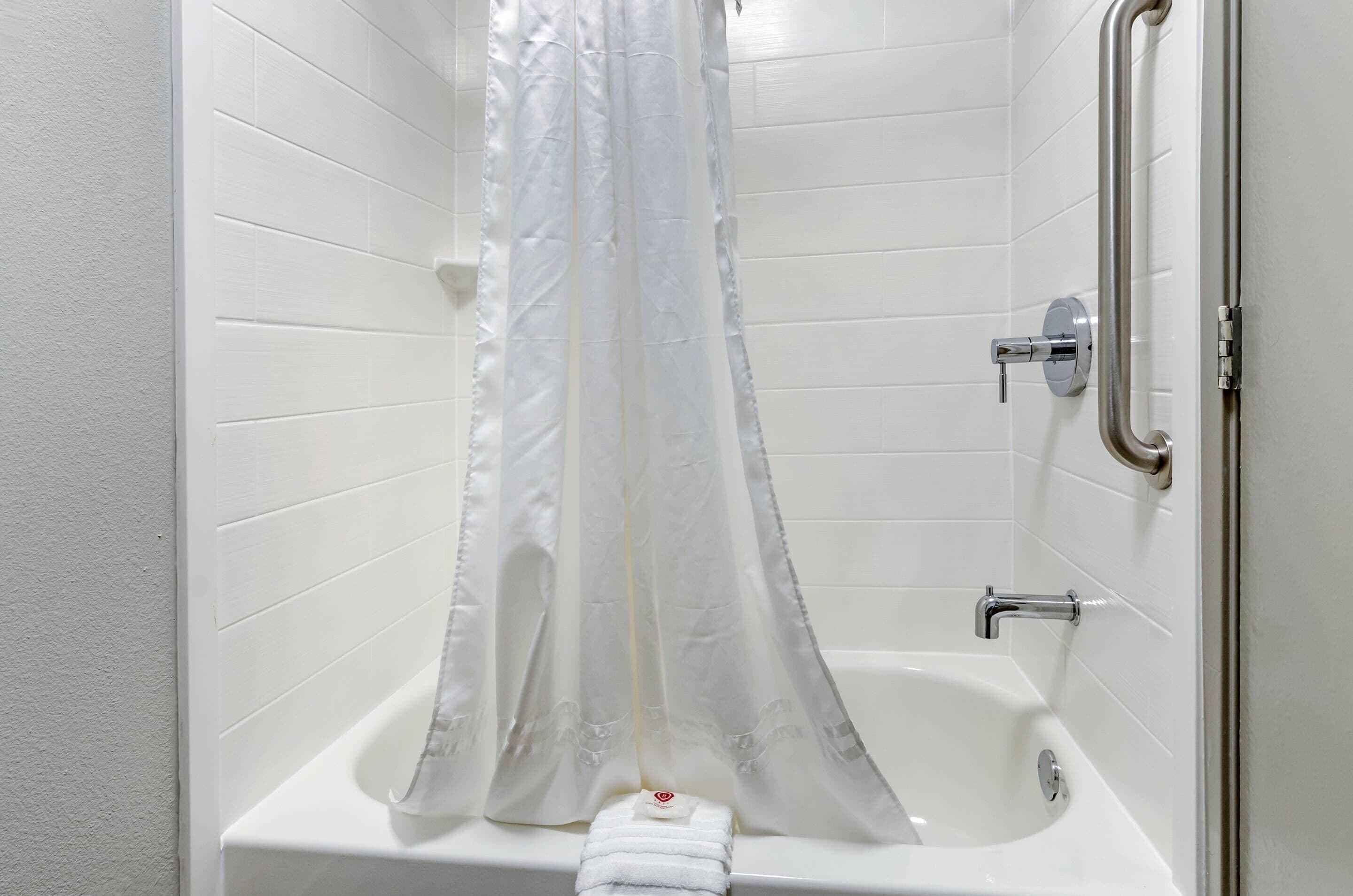 A bathroom with a white bathtub, a shower curtain, and a grab bar.