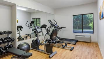 A gym with exercise equipment, a mirror, and a window with a view of trees.