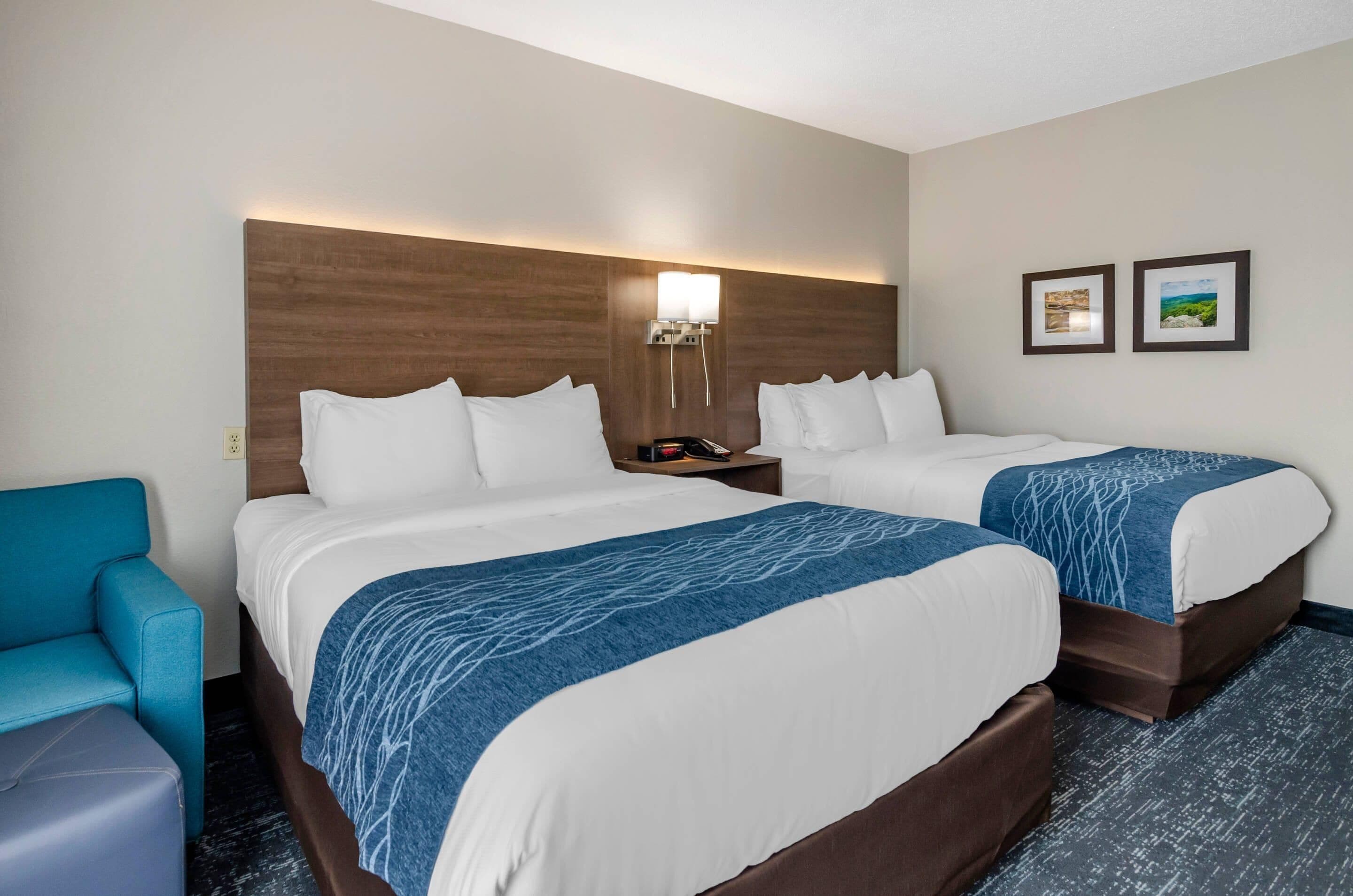 Une chambre d’hôtel avec deux lits, une table de chevet, une lampe et une chaise bleue.