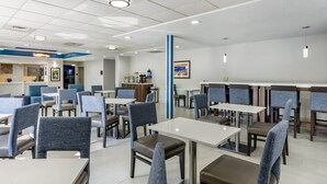 A modern dining area with tables and chairs, a counter with a menu, and a framed picture on the wall. - Comfort Inn & Suites Troutville-Roanoke North (Troutville)