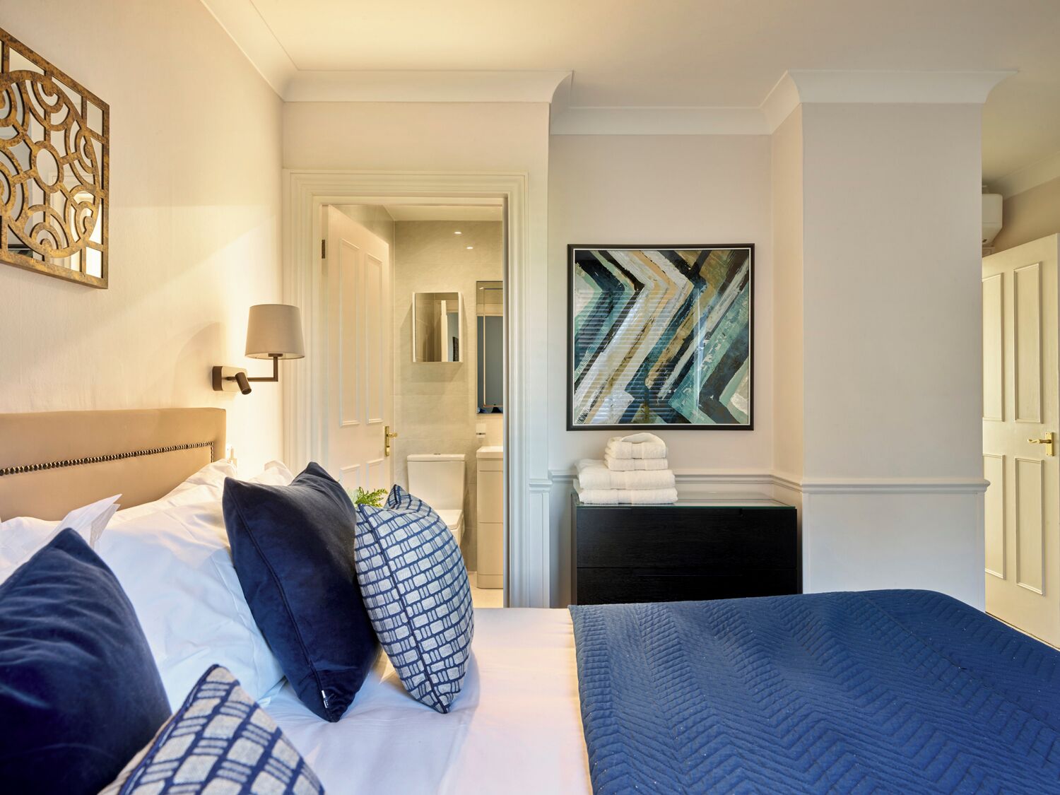 A hotel room with a bed, a nightstand, a mirror, and a painting on the wall.