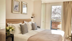 Habitación de hotel con una cama grande, dos cuadros en la pared, una mesita de noche con un jarrón de flores y vistas al exterior a través de una ventana.