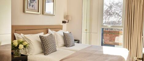 Habitación de hotel con una cama grande, dos cuadros en la pared, una mesita de noche con un jarrón de flores y vistas al exterior a través de una ventana.