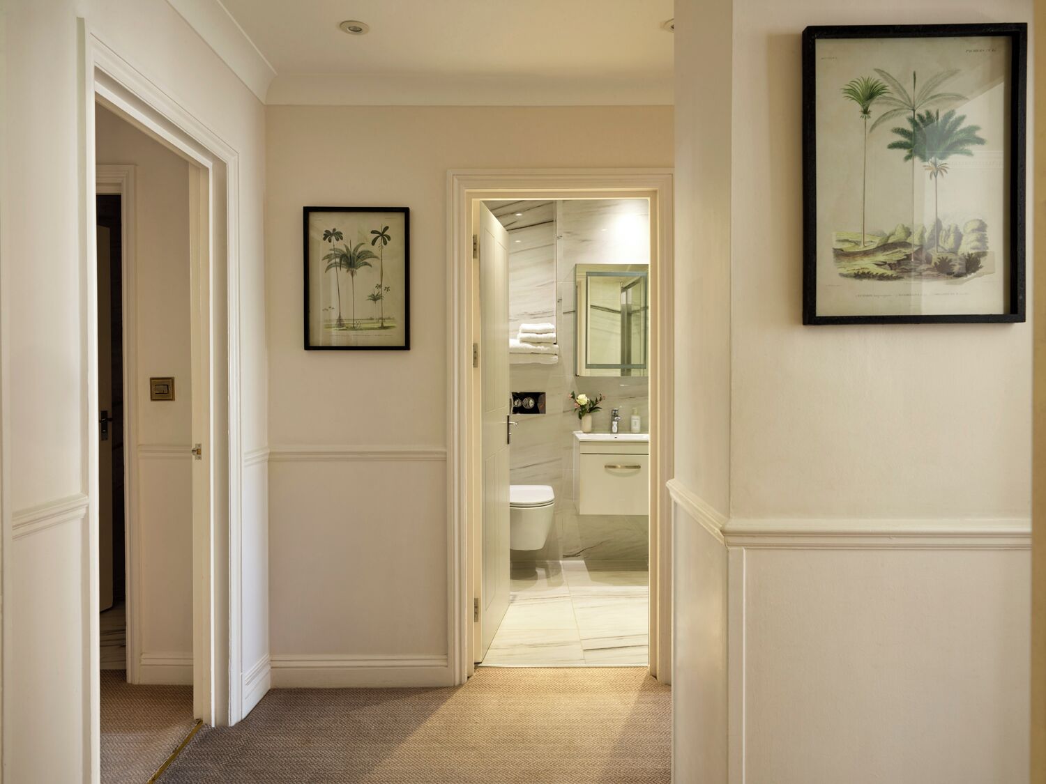 A hallway leading to a bathroom with a toilet, sink, and mirror.