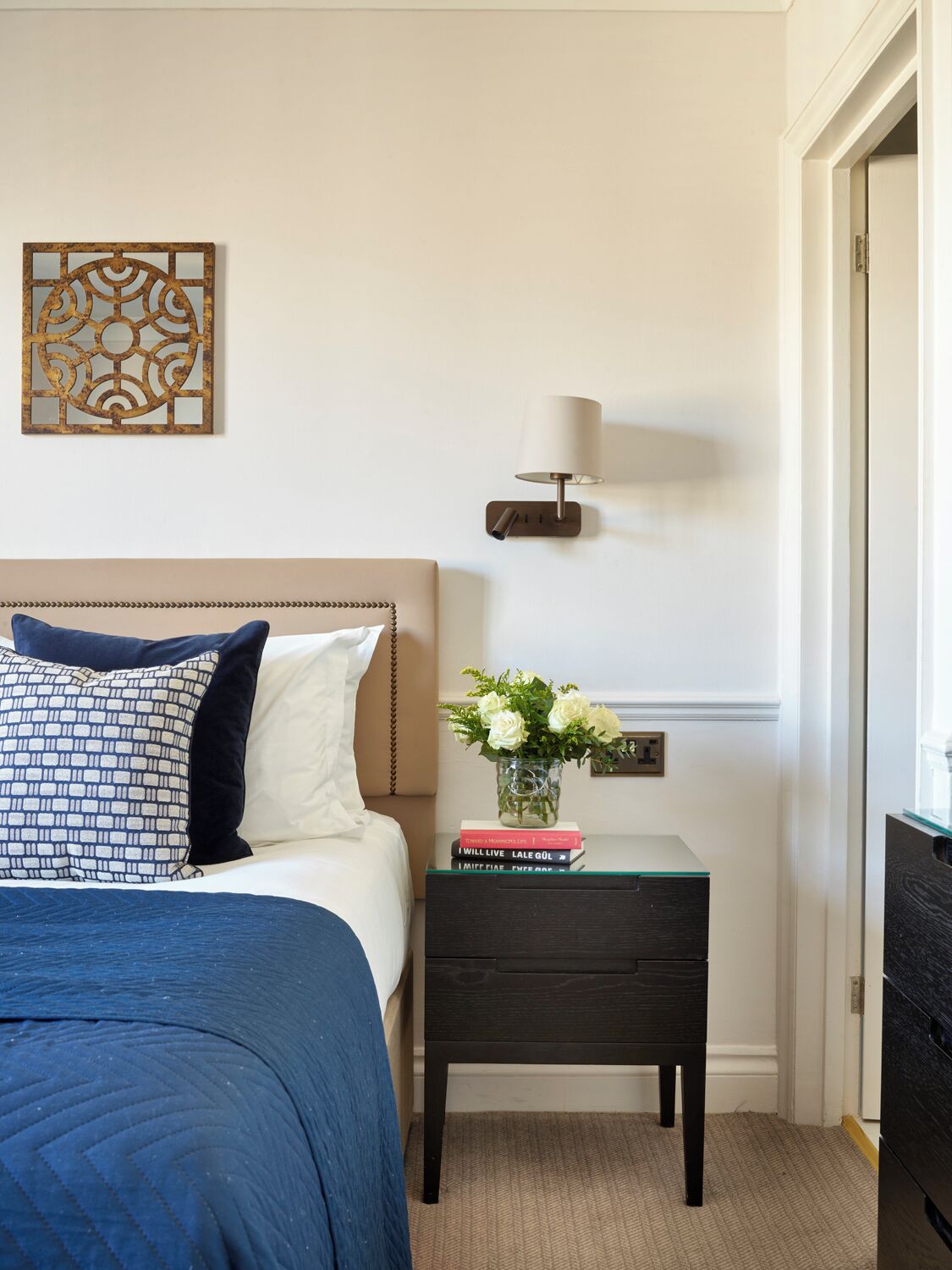 A bedroom with a bed, bedside table, lamp, and decorative wall piece.