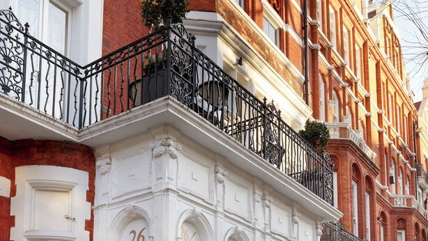 Un edificio histórico con fachada blanca, barandillas de hierro negro y el número 26 en la puerta.