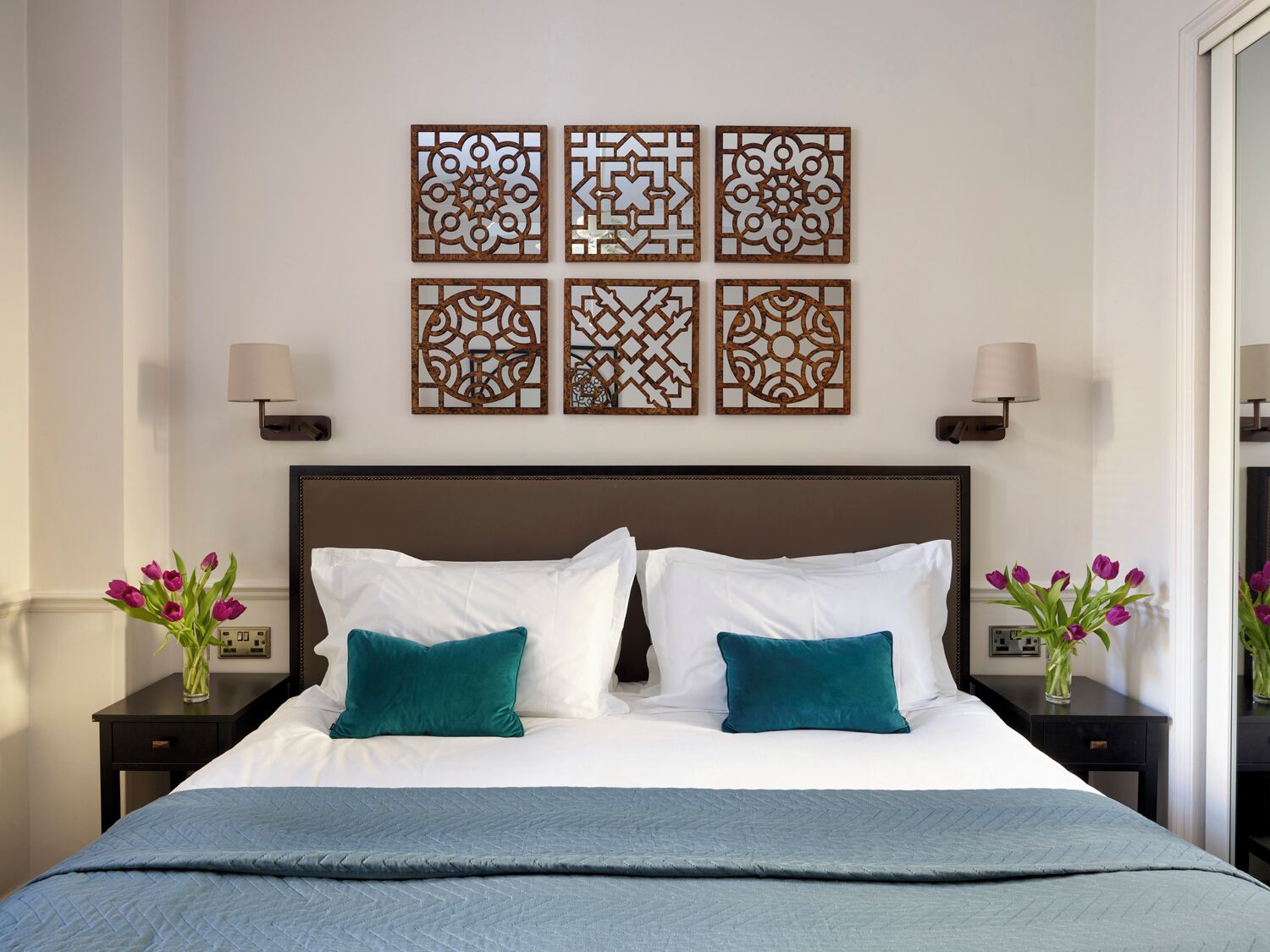 A neatly made bed with white and teal pillows, a teal blanket, and decorative wall art above.