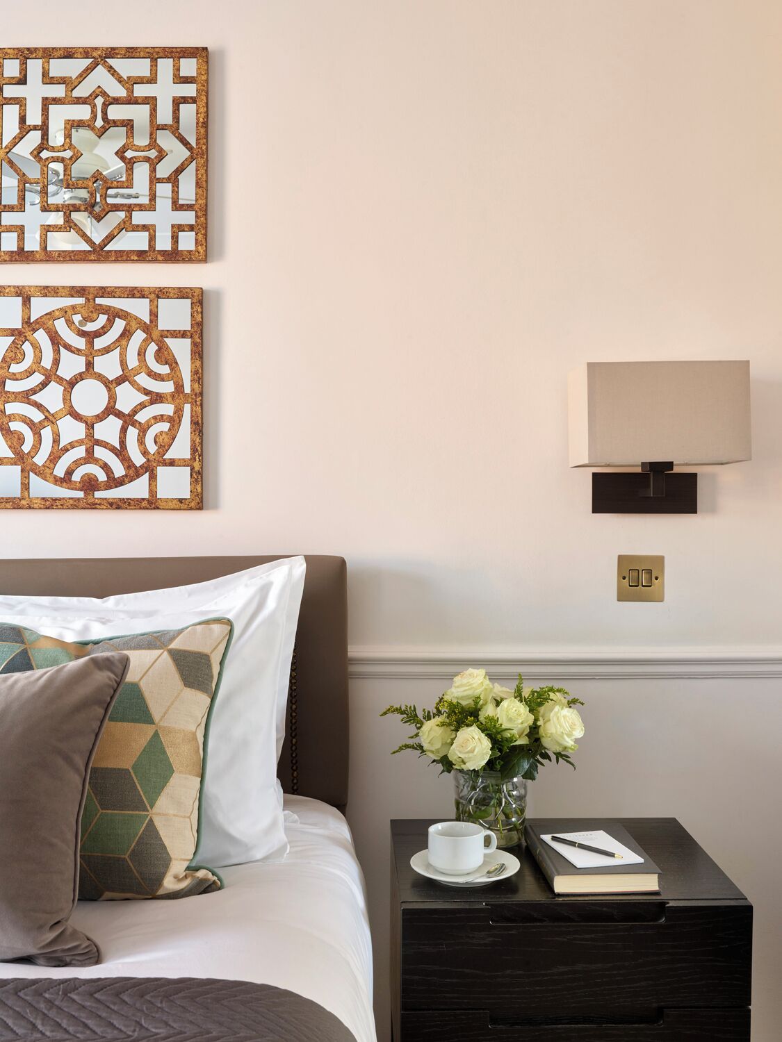 A neatly arranged hotel room with a bed, a nightstand with a vase of flowers, and two wall-mounted decorative panels.