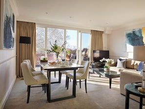 A modern living room with a dining area, large windows, and a flat-screen TV.