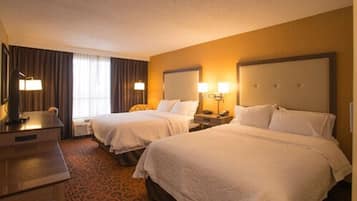 A hotel room with two beds, a desk, and a lamp.