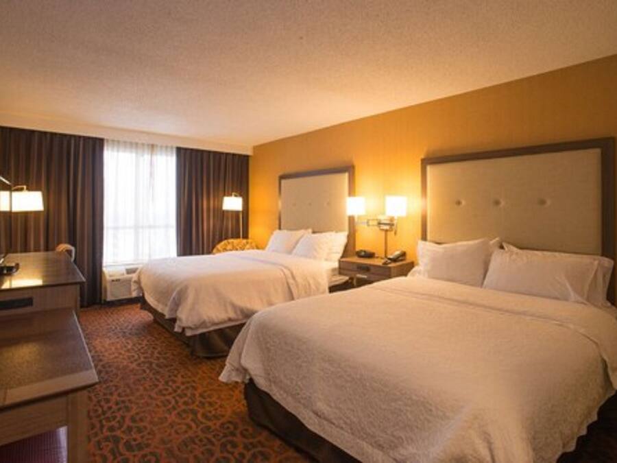 A hotel room with two beds, a desk, and a lamp.