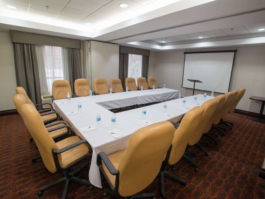 Uma sala de conferências com uma mesa comprida, várias cadeiras, garrafas de água, uma tela de projetor e um quadro branco.