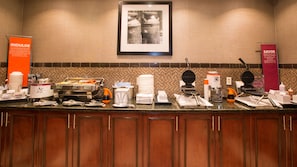 A buffet setup with various food stations, including a waffle maker, coffee machine, and a sign promoting a snack stack.