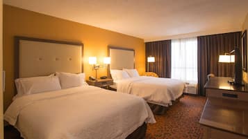 Habitación de hotel con dos camas, un escritorio y una ventana con cortinas.