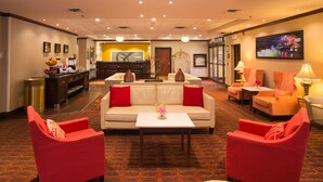 A hotel lobby with a reception desk, seating area with a sofa and chairs, and a carpeted floor.