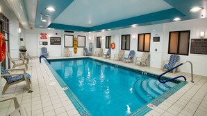 An indoor swimming pool with clear blue water, surrounded by lounge chairs and safety signs.