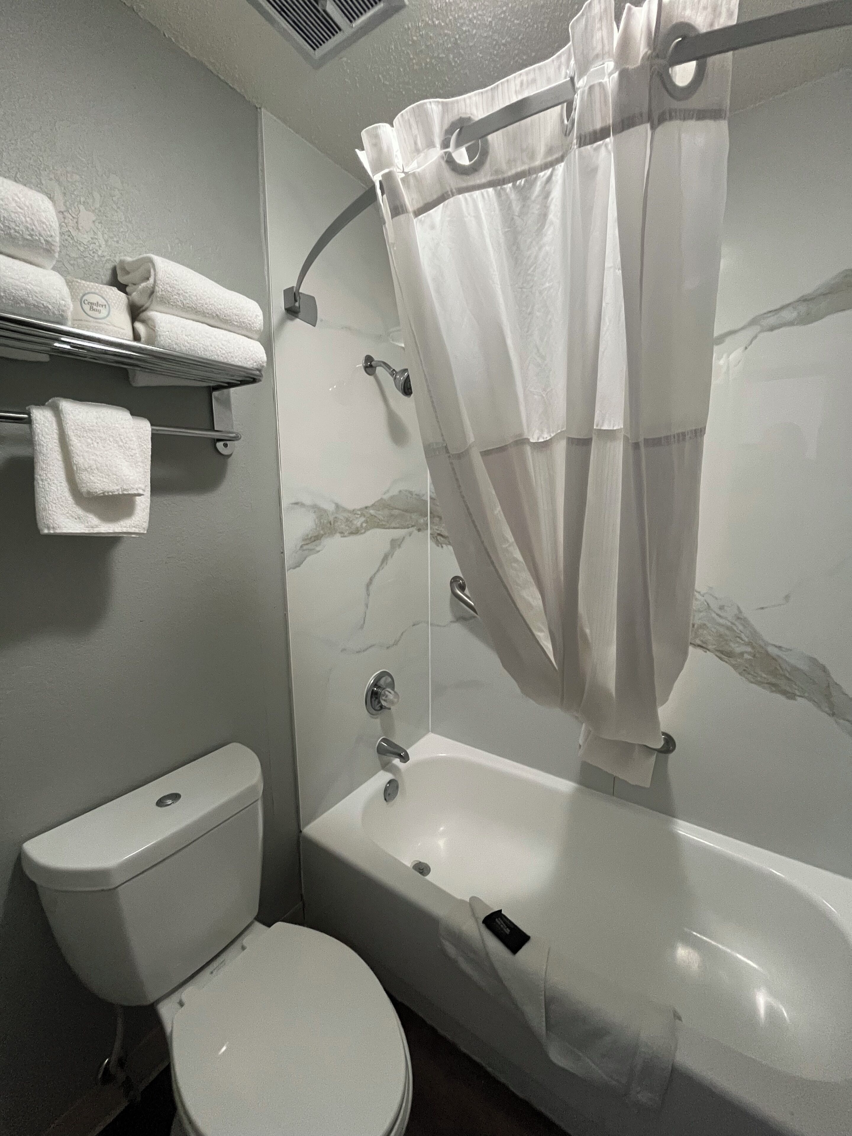 A bathroom with a toilet, a bathtub, a shower curtain, and a towel rack with towels.