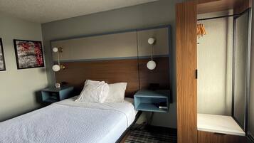 Habitación de hotel con una cama grande, una mesita de noche, un estante en la pared y una puerta con espejo.