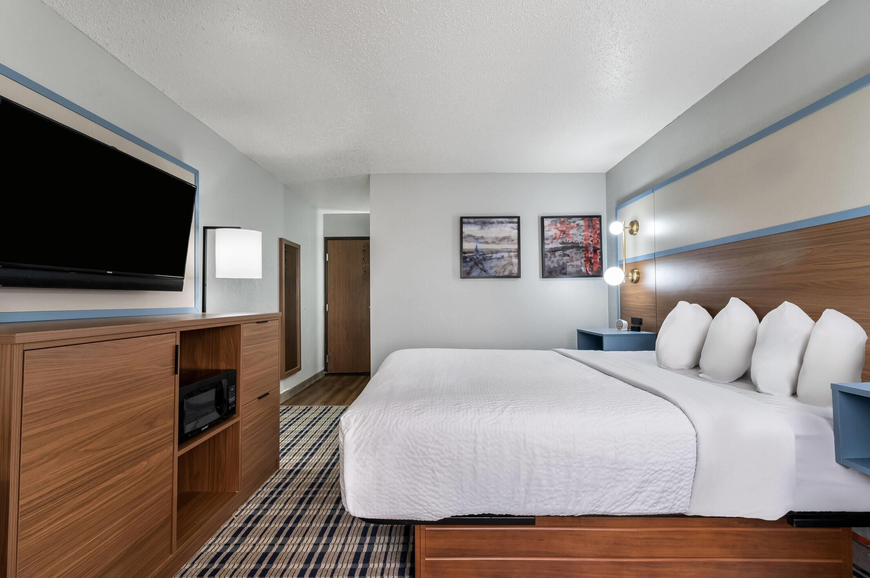 Een hotelkamer met een groot bed, een flatscreen televisie, een houten kastje met een magnetron, en een kamerbreed tapijt met een patroon.