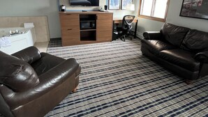 A living room with a sofa, a television, a desk, and a window. - AmericInn by Wyndham Cloquet (Cloquet)