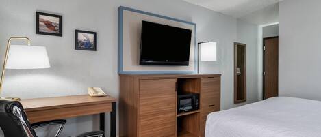 A hotel room with a bed, desk, chair, TV, and a microwave.
