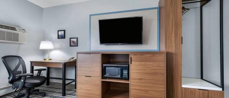 Une chambre d’hôtel équipée d’un bureau, d’une chaise, d’une télévision, d’un four à micro-ondes et d’une armoire.