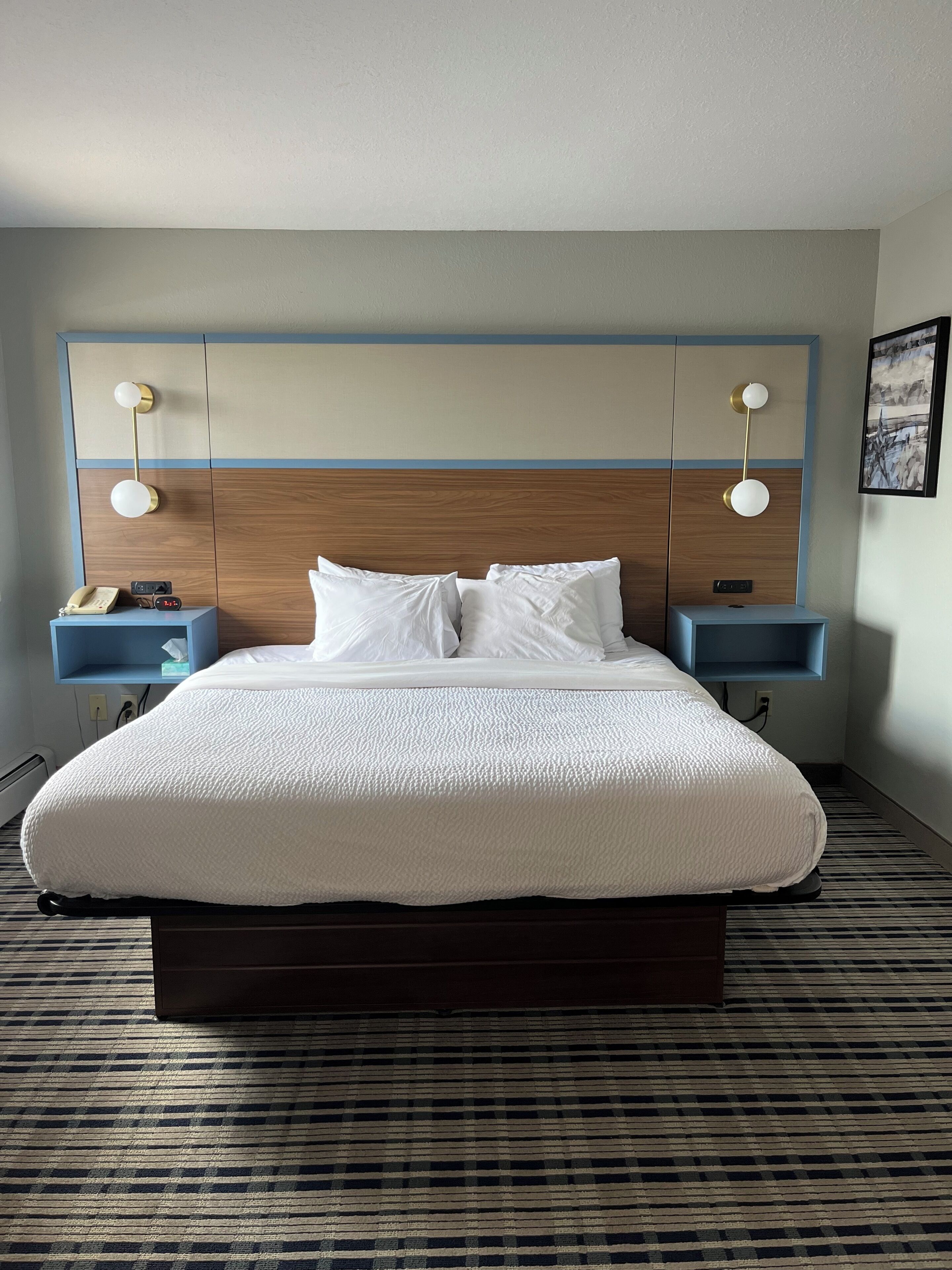 A hotel room with a large bed, two bedside tables with lamps, a wooden headboard, and a patterned carpet.