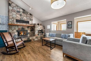 Ein Wohnzimmer mit Kamin aus Stein, einem Schaukelstuhl, einer Couch und einem Couchtisch.
