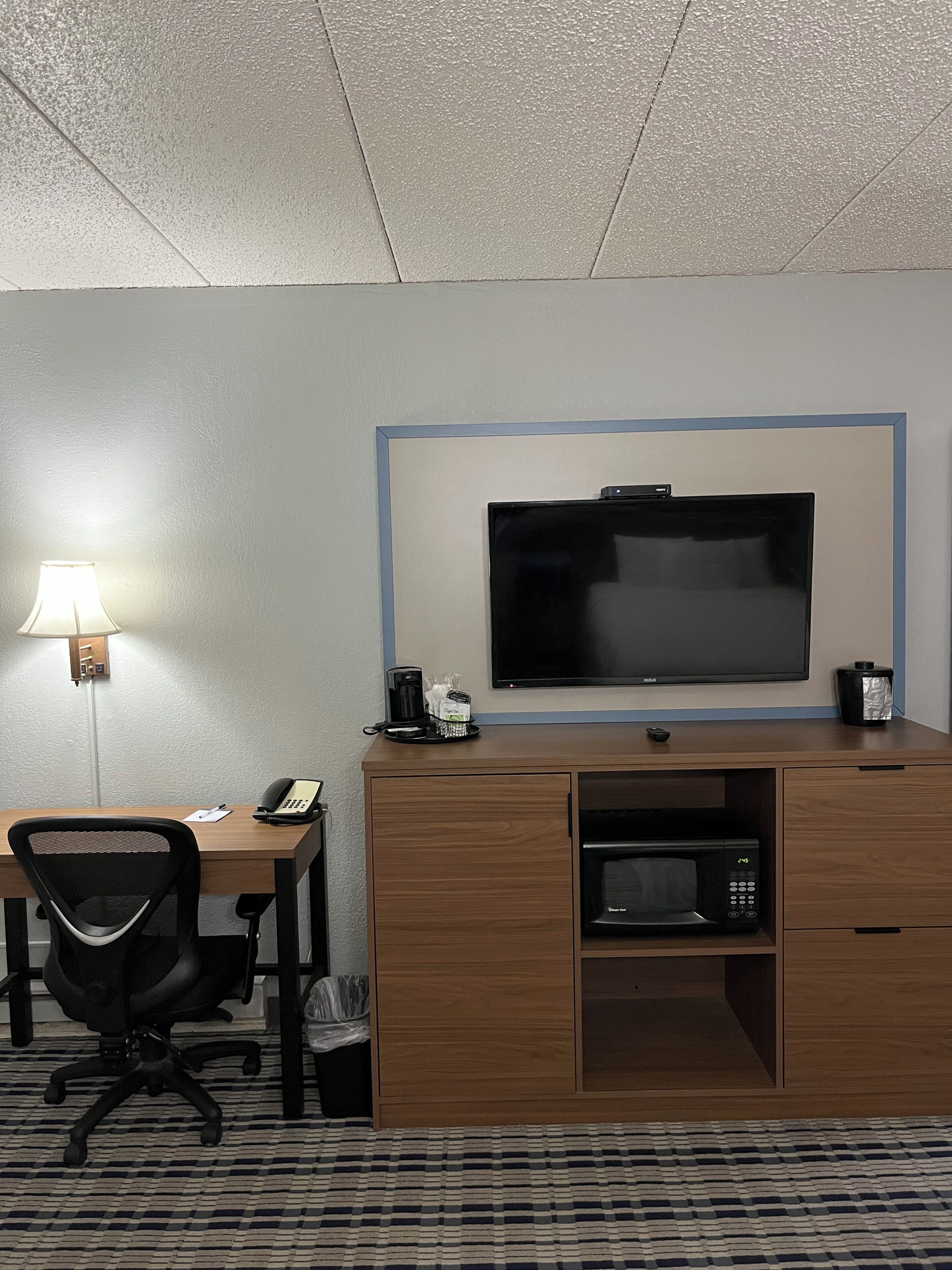 Habitación de hotel con escritorio, silla, televisión, cafetera, microondas y un cubo de basura.