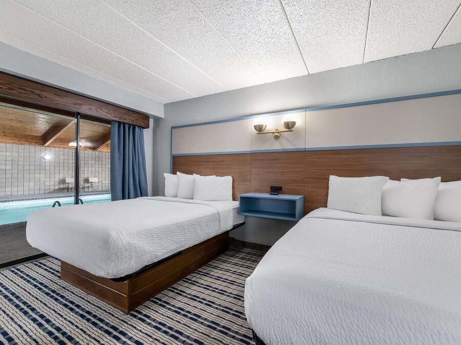 A hotel room with two beds, a large window with a view of a pool, and a wooden ceiling.