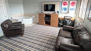 A living room with a sofa, a chair, a coffee table, a TV, a desk, and a patterned carpet. - AmericInn by Wyndham Cloquet (Cloquet)