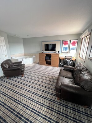 A living room with a sofa, a chair, a coffee table, a TV, a desk, and a patterned carpet. - AmericInn by Wyndham Cloquet (Cloquet)