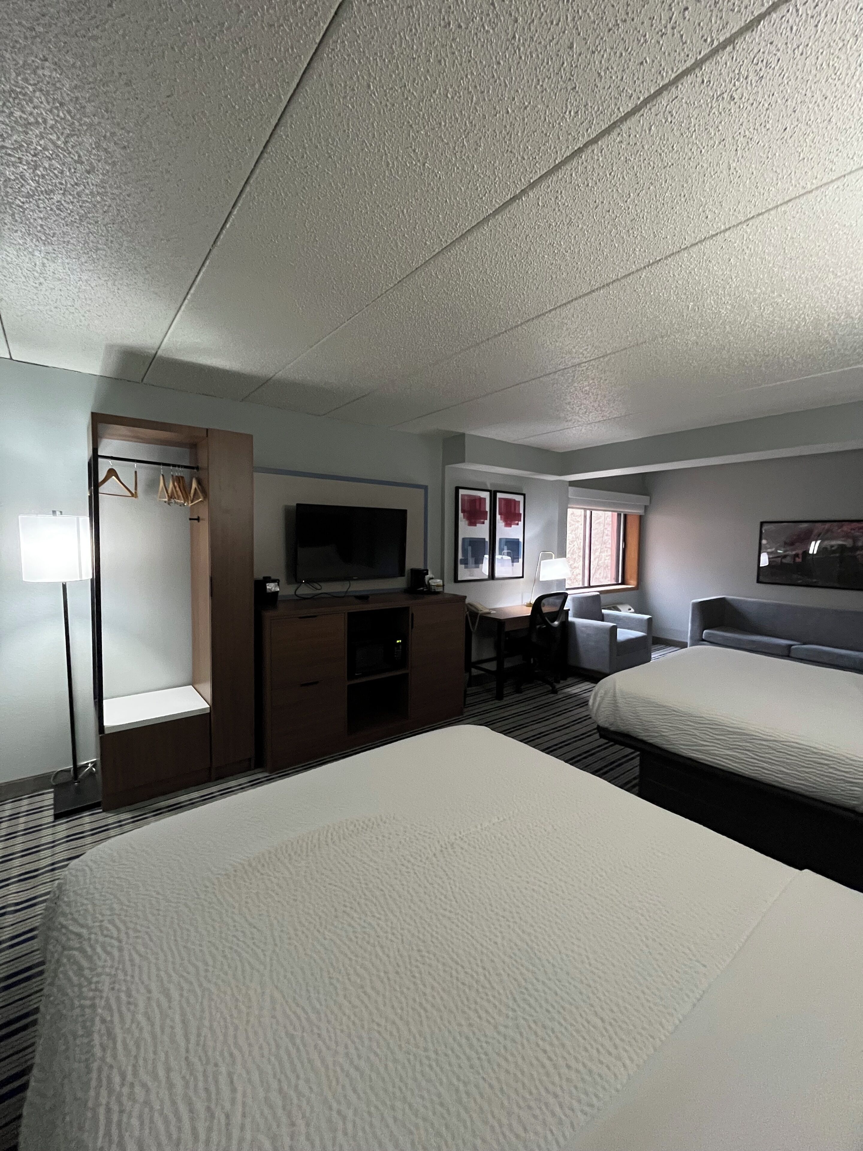 A hotel room with two beds, a desk, a chair, a TV, and a wardrobe.