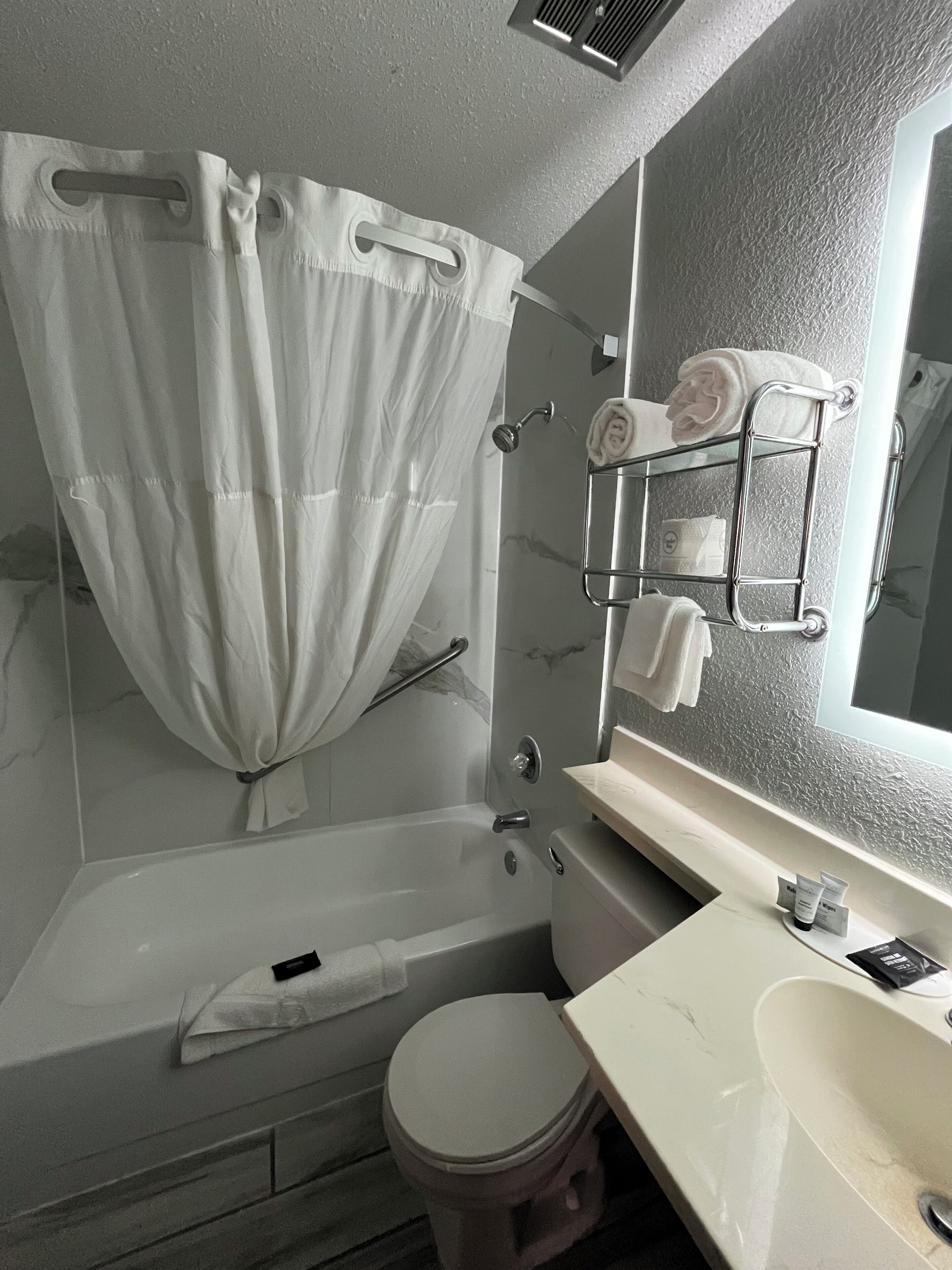 A bathroom with a shower curtain, a glass shower enclosure, a toilet, a sink, and a towel rack with towels.