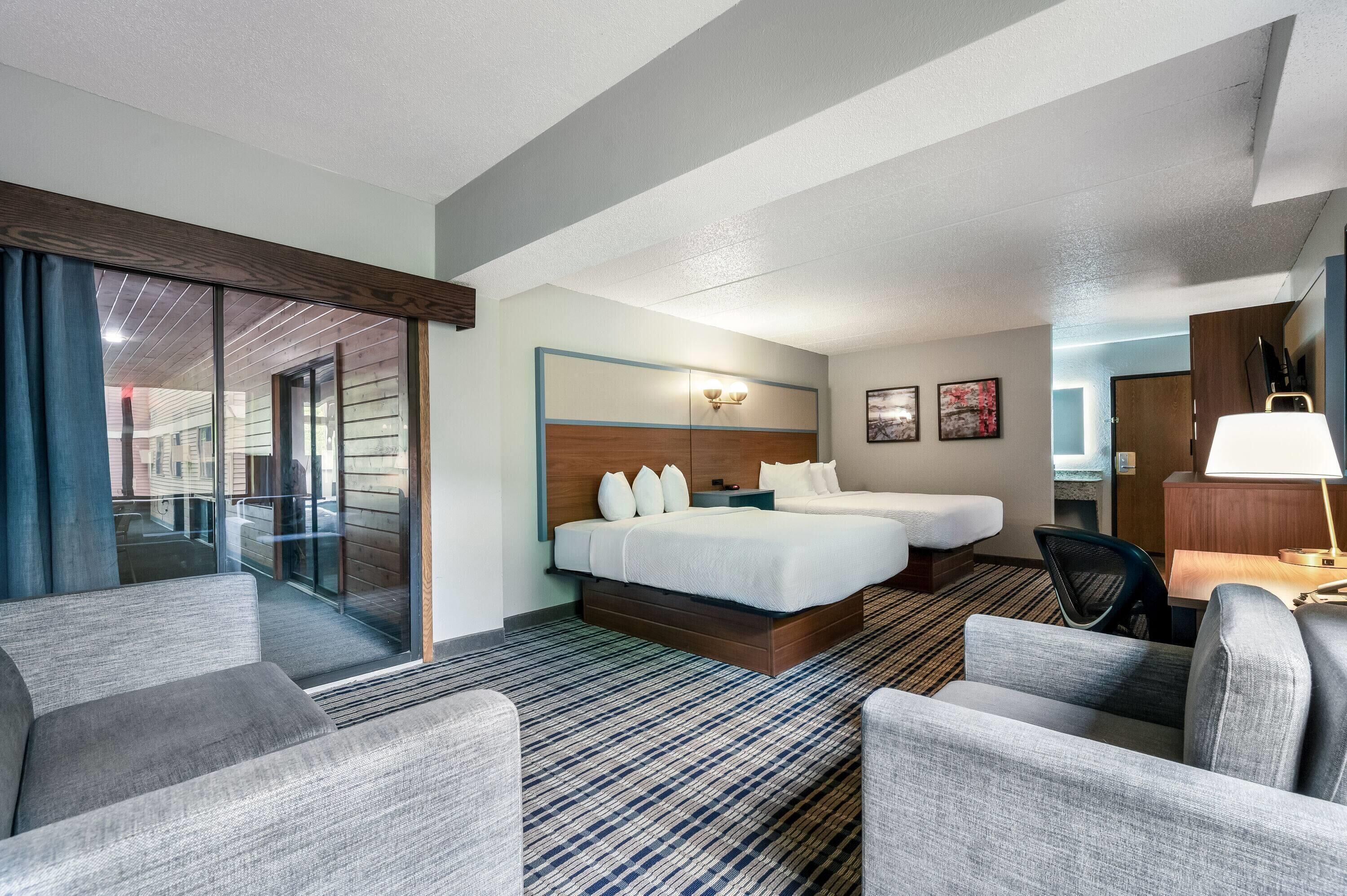 Une chambre d’hôtel avec un grand lit, deux tables de chevet, un bureau avec une chaise, un canapé et une vue sur l’extérieur.