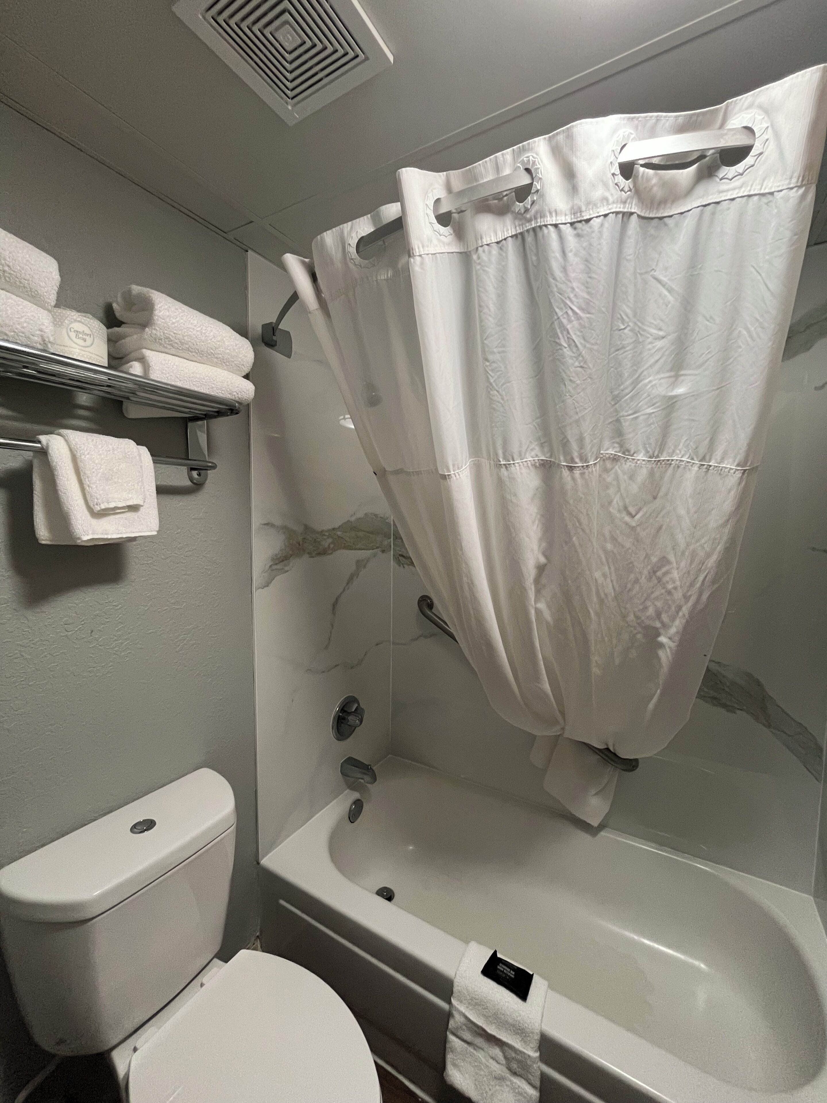 A bathroom with a bathtub, toilet, and towel rack with towels.