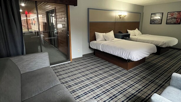 A hotel room with a large bed, a sofa, a small table, and a view of the outside. - AmericInn by Wyndham Cloquet (Cloquet)