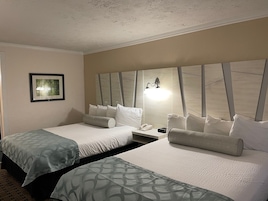 Habitación de hotel con dos camas, una mesita de noche, un cuadro enmarcado y una lámpara de pared.