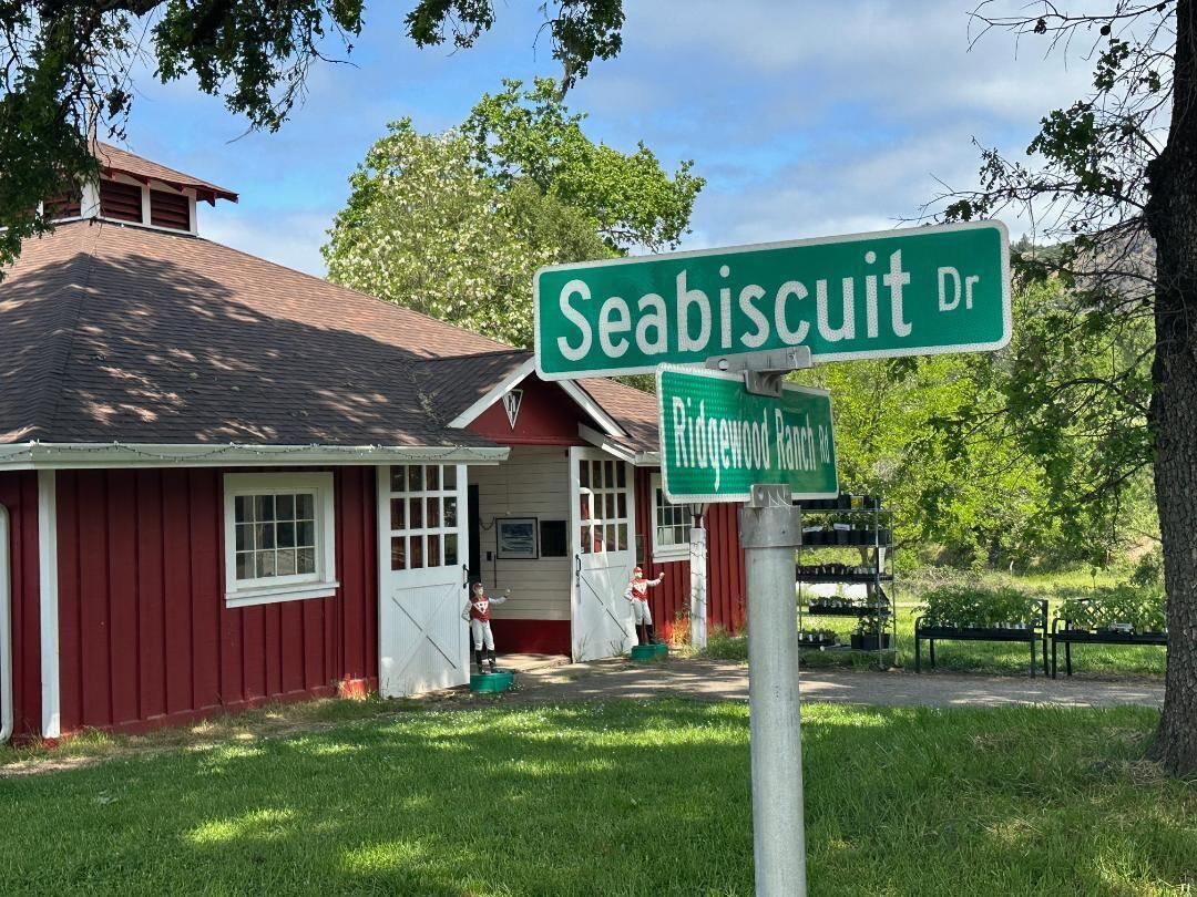 A red building with a white door and windows, a green street sign for Seabiscuit Dr, and a smaller sign for Ridgewood Ranch Rd.