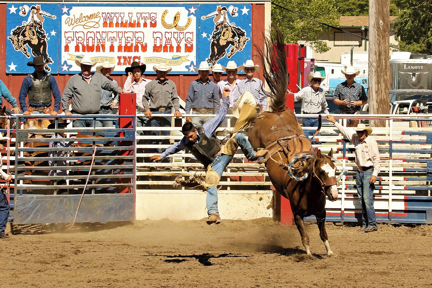 A rodeo event with a bull and a rider in action, surrounded by spectators and a sign that reads "Welcome Willits Frontier Days."